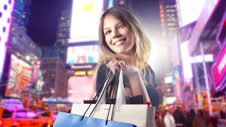 Smiling shopper holding shopping bags in the city at night.