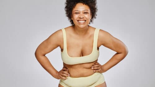 Woman with pear-shaped body wearing underwear smiles.