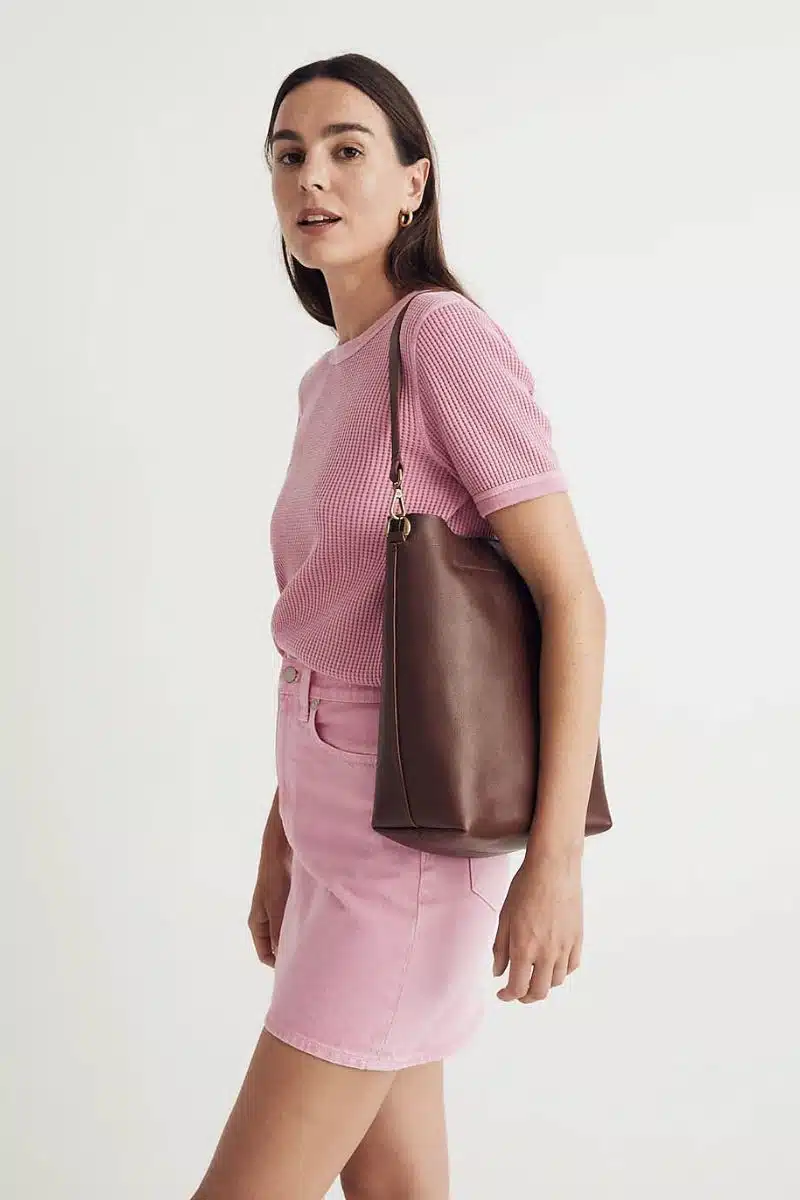 Woman holds large leather tote bag by Madewell over her shoulder. 