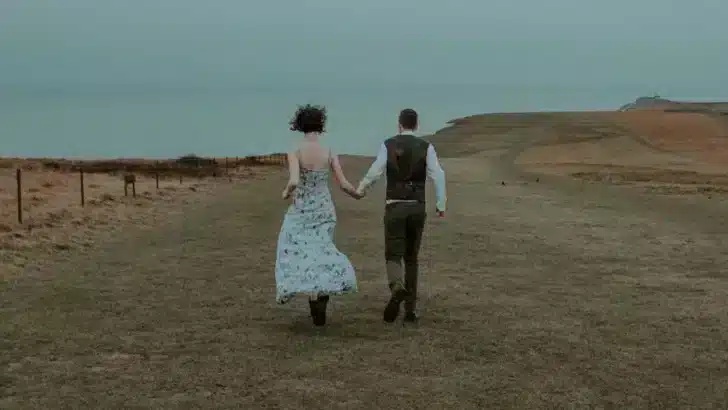 Couple walk away from camera in outdoor landscape.
