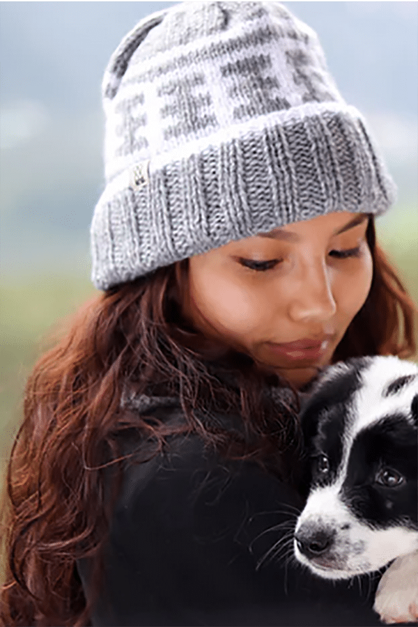 Woman holding puppy wears knit beanie from charity brand Fazl.