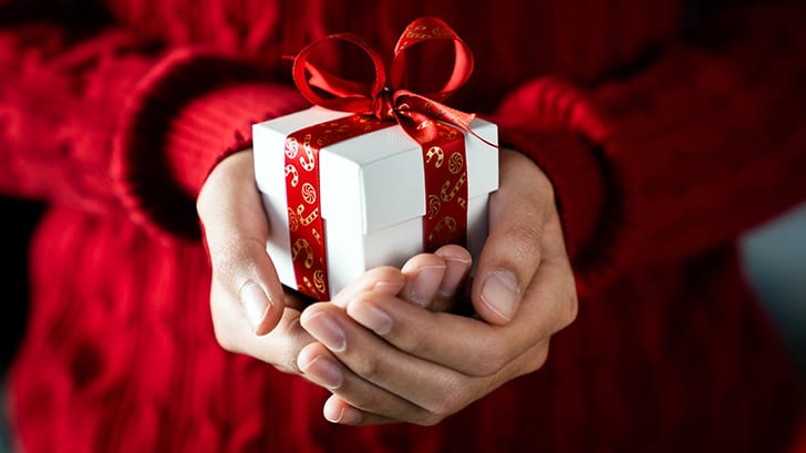 Woman's hands hold small gift in a white box with a red bow.