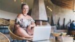 Smiling woman uses laptop to shop best online women's clothing stores.