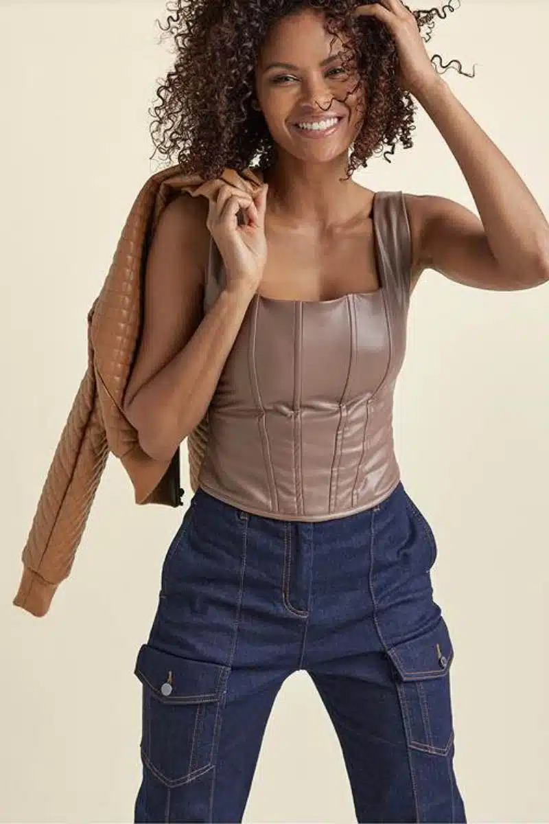 Smiling model wears leather corset top with jeans. 
