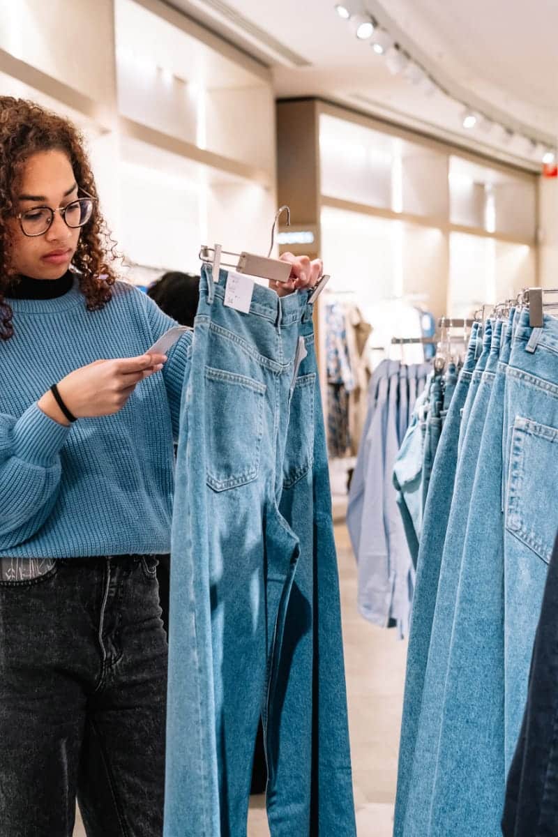 Woman checks price tag of jeans to represent cost per wear concept.