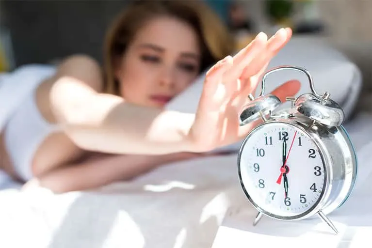 Woman in bed turning off the alarm clock