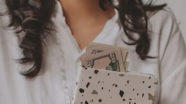 Close-up of woman holding folder with cash sticking out of it.