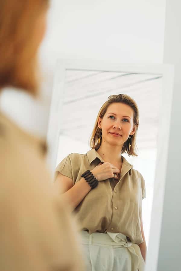 Woman looking at her outfit in the mirror, thinking, "I have no style." 