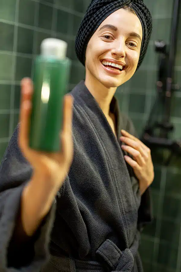 Woman holding bottle of natural hair care in the shower.