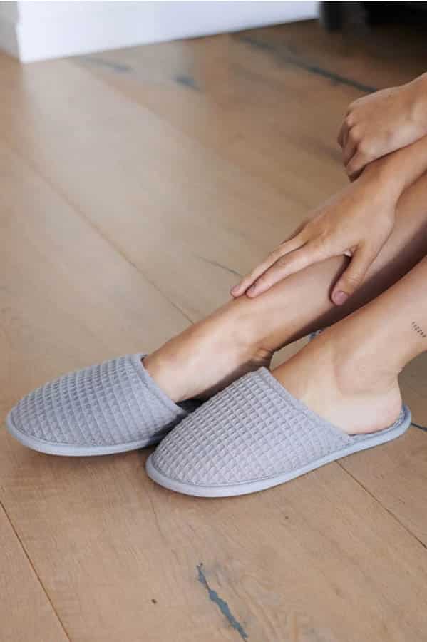 Close-up of woman's legs wearing gray waffle knit chic slippers.