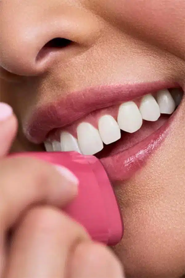Close up of woman applying tinted lip balm while smiling. 