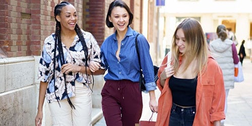 Group of trendy woman smile together while walking with shopping bags outside.
