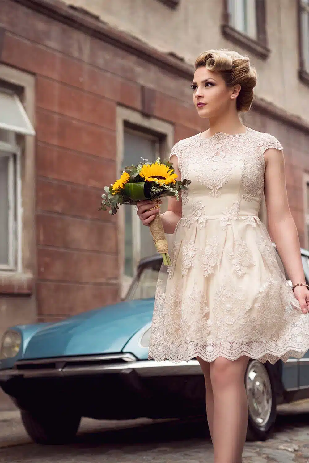 Woman walks on street wearing retro wedding dress and holding flowers.