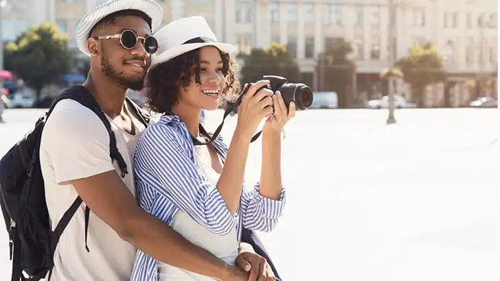 Couple wearing stylish honeymoon outfits smile while taking a photo.