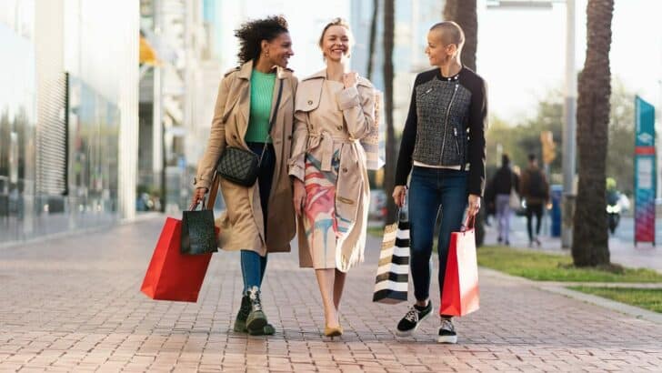 Three women wearing street style fashion holding shopping bags outside.