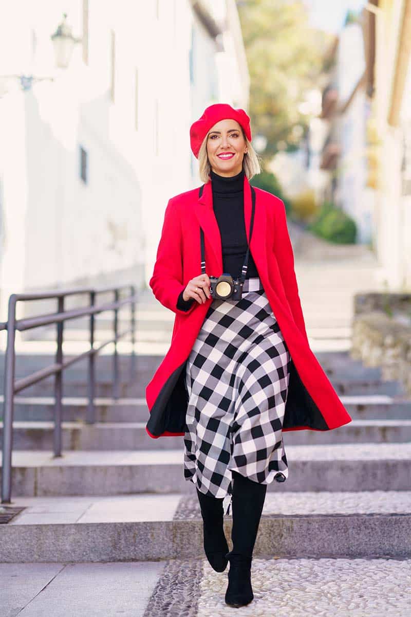 Woman wearing bold outfit with red beret and jacket walks outside.