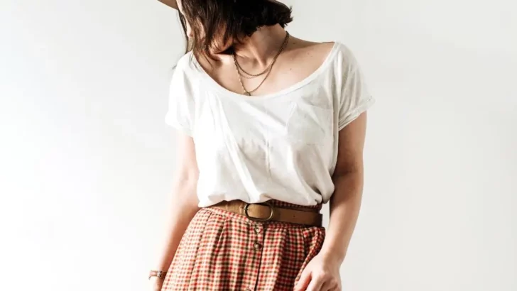 Model wears pleated pants and white top in front of white background.